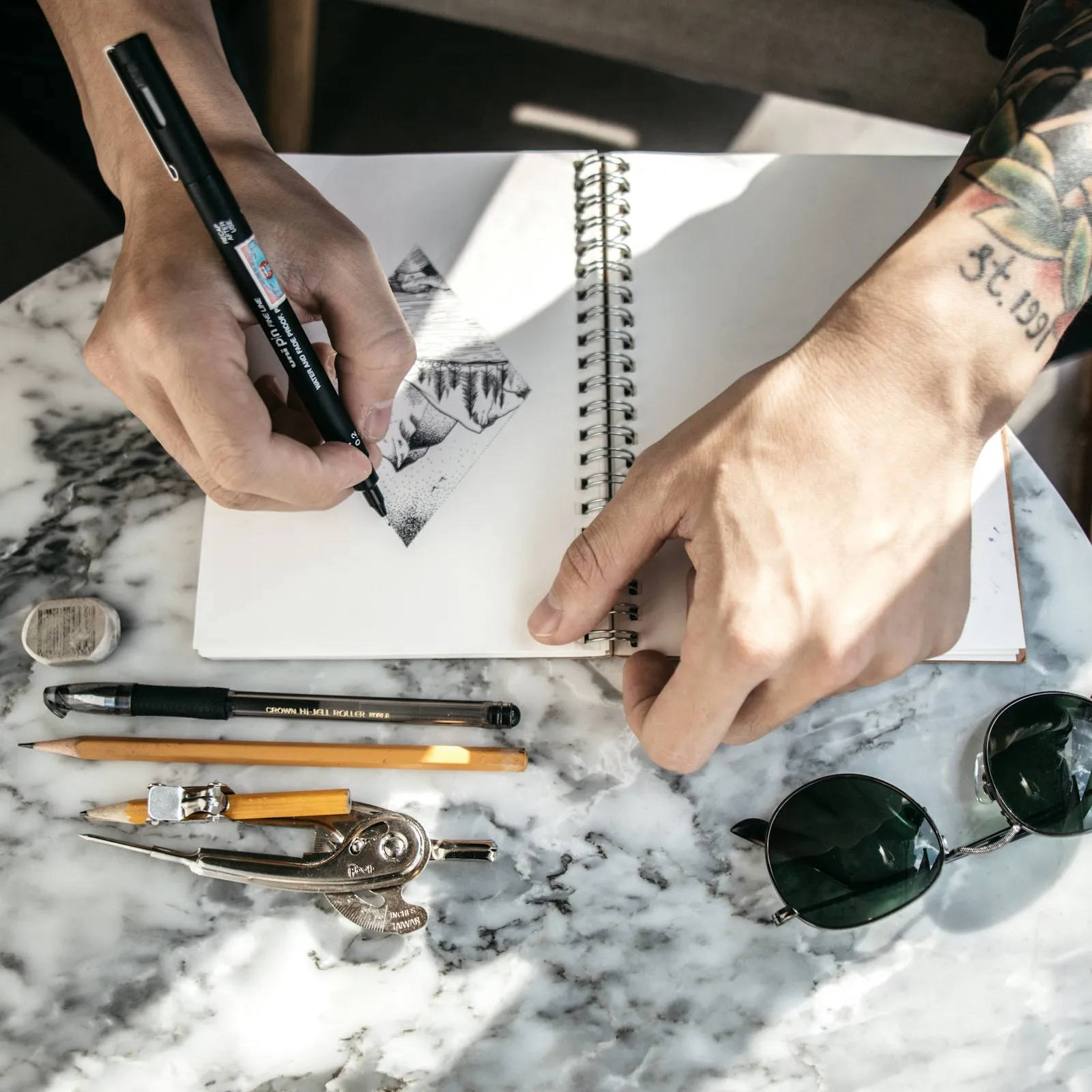 Hands sketching in a notebook with drafting tools on the desk